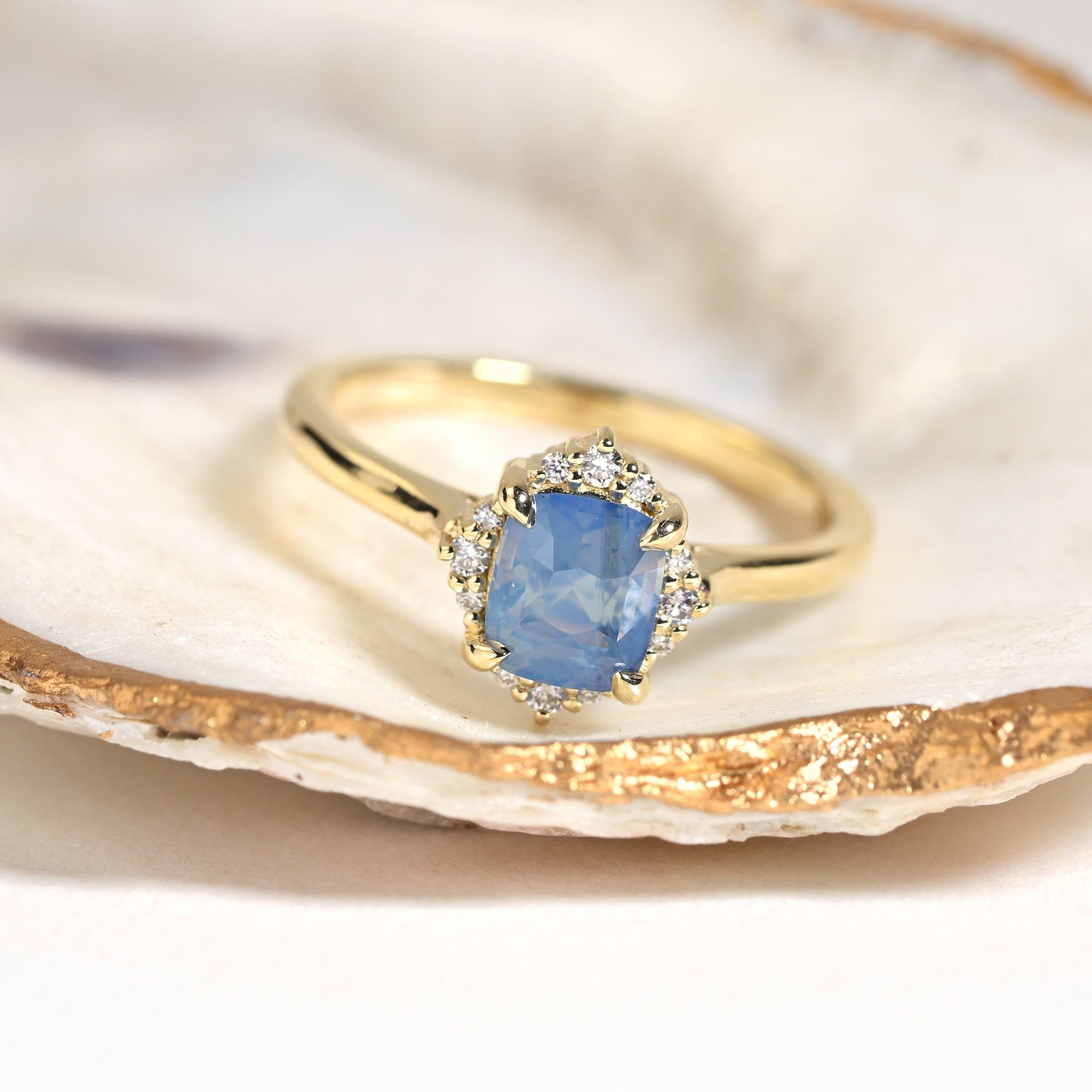 14k yellow gold diamond halo engagement ring with a opalescent blue cushion sapphire