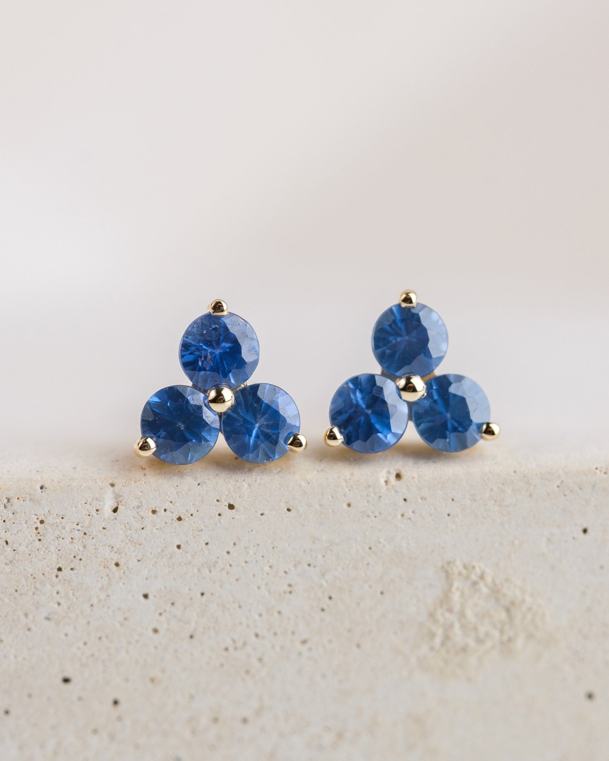 14k yellow gold stud earrings with 3 blue sapphires arranged in a floral shape