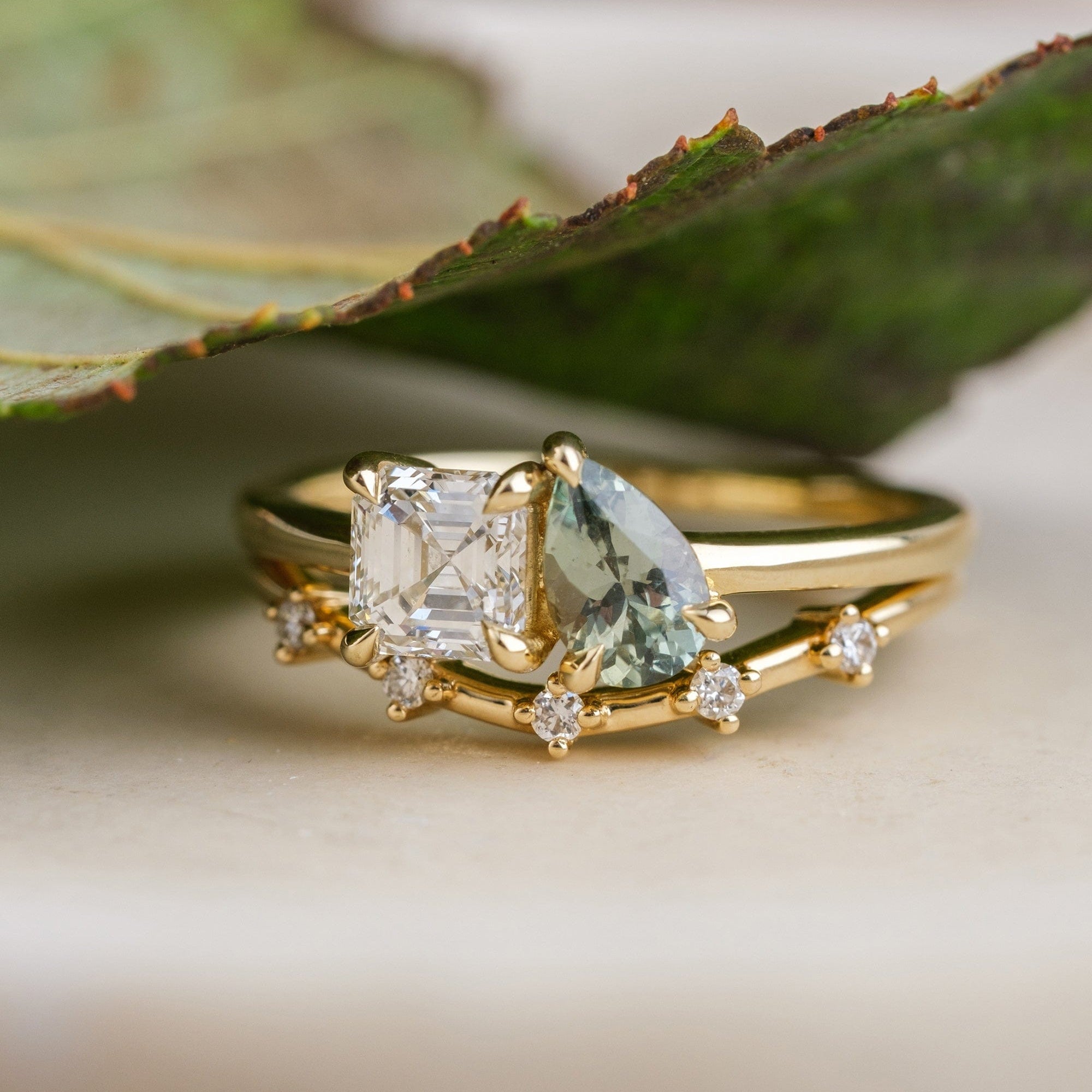 14k yellow gold Toi et Moi ring with an Asscher-cut diamond and sage green pear cut sapphire, paired with a 14k yellow gold band with 5 diamonds