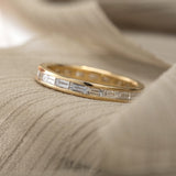 Channel set baguette diamond wedding band in 14k yellow gold sitting on a beige background