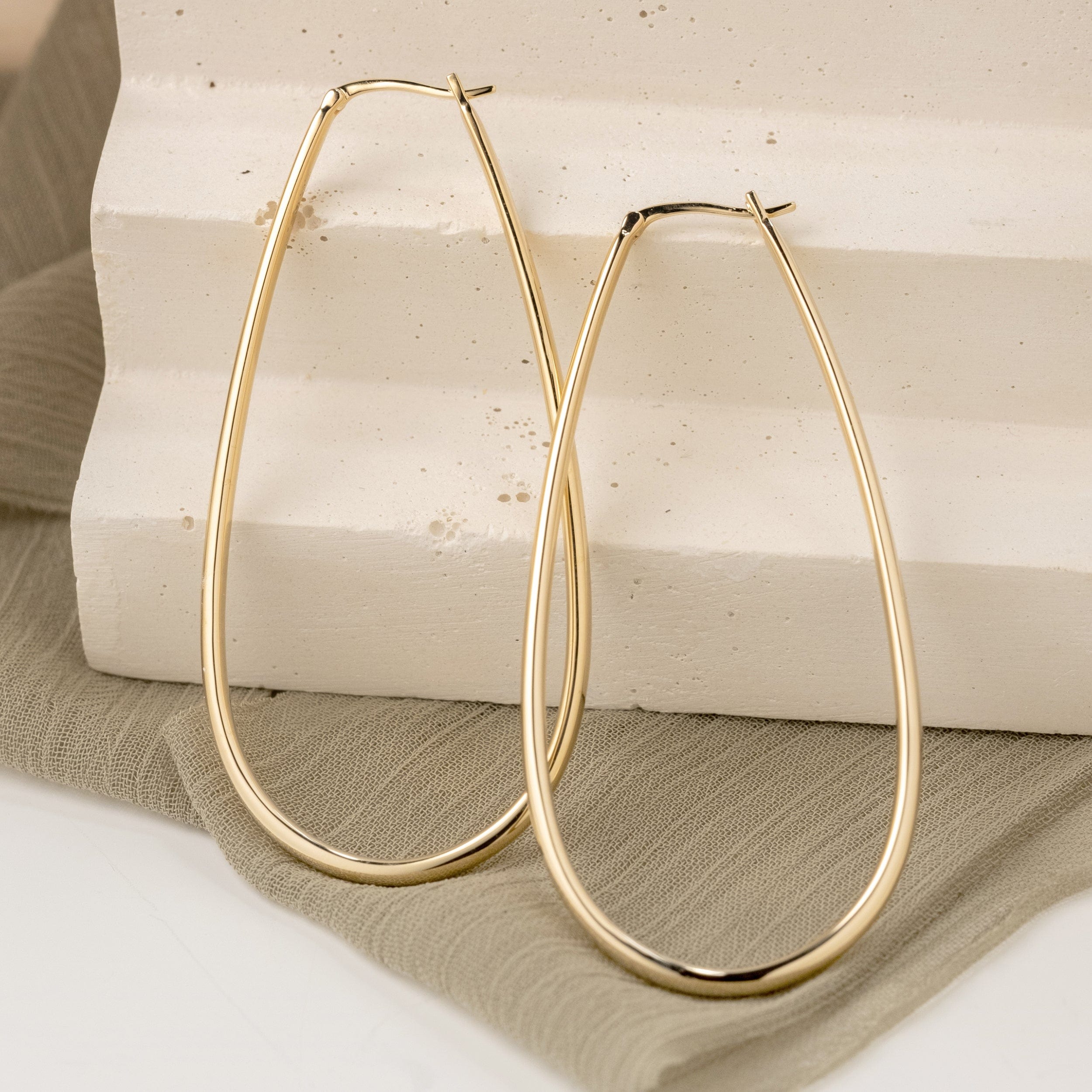 Small yellow gold oval shaped hoop earrings leaning against clay steps